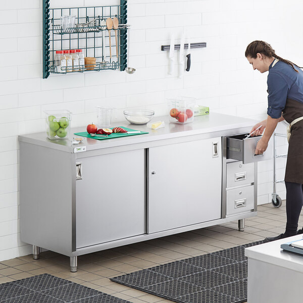 A woman opening a drawer in a stainless steel kitchen table.