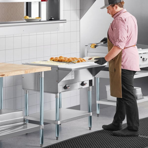 A man wearing a brown apron using a ServIt liquid propane steam table in a professional kitchen.