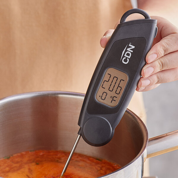 A person using a CDN ProAccurate digital folding thermocouple thermometer to measure the temperature of a pot of soup.