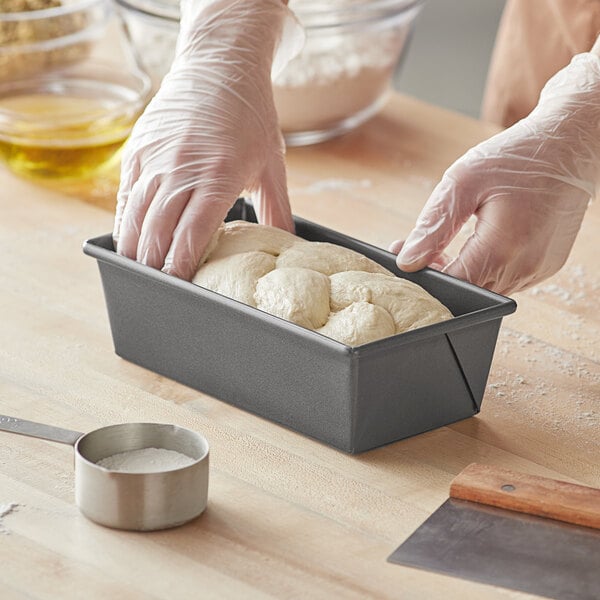 A person's gloved hands putting dough into a Choice Quantum2 loaf pan.
