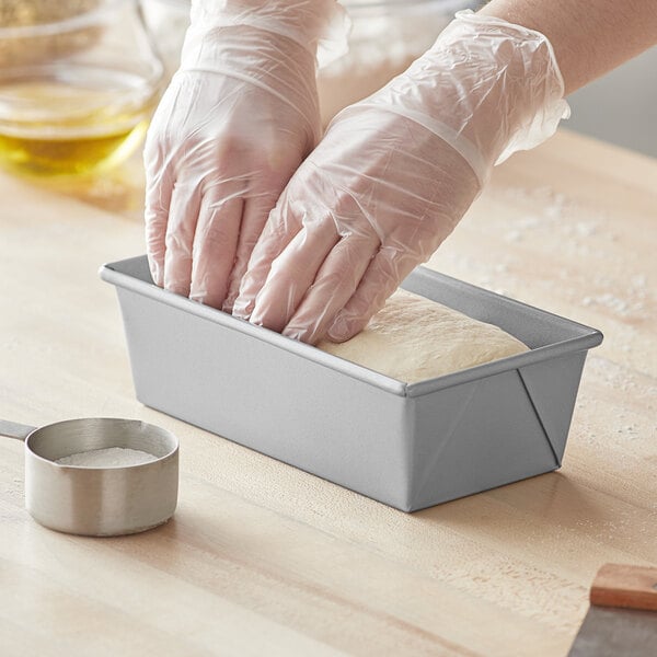 A pair of hands wearing plastic gloves kneading dough in a Baker's Mark aluminized steel loaf pan.