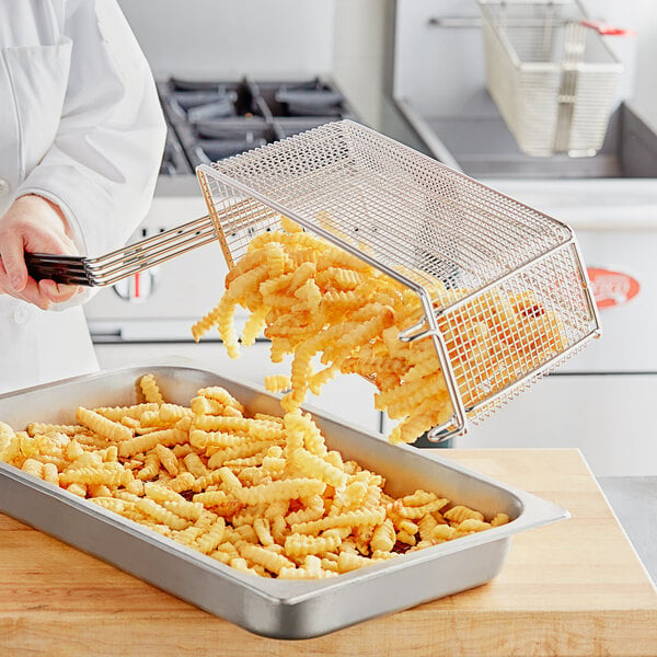 A person using a Pitco triple fryer basket to fry french fries.