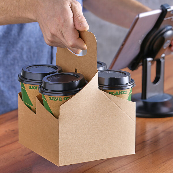 A hand holding a Choice drink carrier with three cups inside.