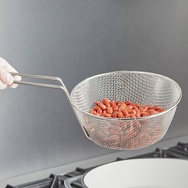 A hand holding a Choice fine mesh culinary basket full of red beans over a pot.