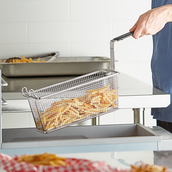 A person holding a 13 1/4" x 4 1/8" Triple Fryer Basket filled with fries.