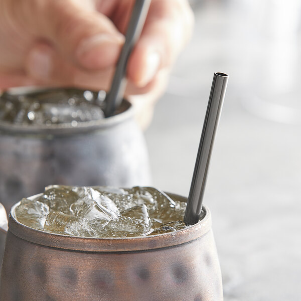 A person holding an Acopa black stainless steel reusable straw in a drink.