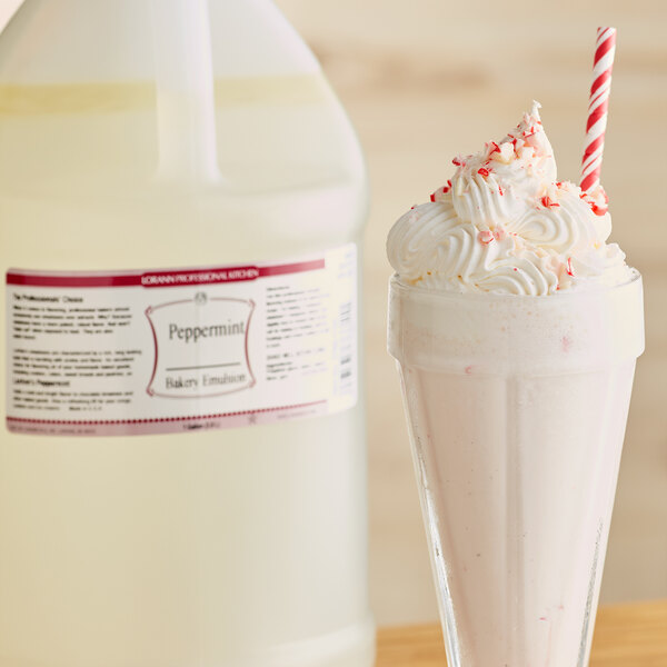 A glass of milkshake with whipped cream next to a bottle of LorAnn Oils All-Natural Peppermint Bakery Emulsion.