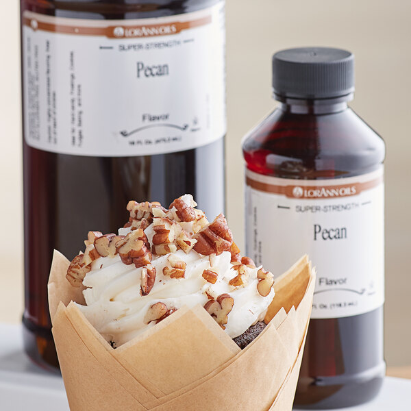 A cupcake in a brown wrapper with whipped cream and pecans next to a bottle of LorAnn Pecan Super Strength Flavor.