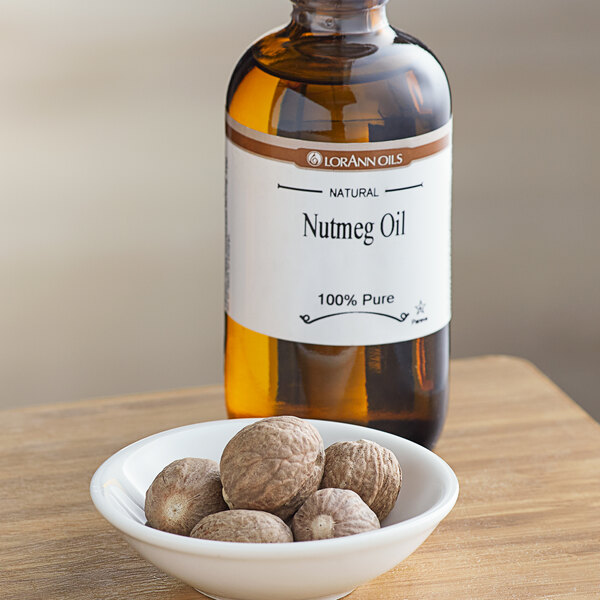 A bowl of nuts in front of a bottle of LorAnn Oils All-Natural Nutmeg Super Strength Flavor.