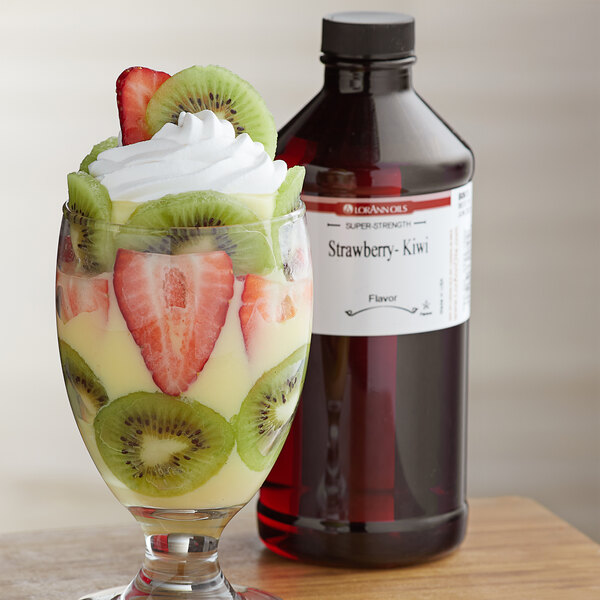A glass of fruit with a red liquid next to a bottle of LorAnn Oils Strawberry Kiwi flavor.