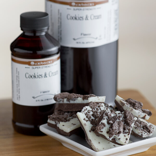 A bottle of LorAnn Oils Cookies and Cream flavoring on a counter close to a white and black dessert with chocolate chips.