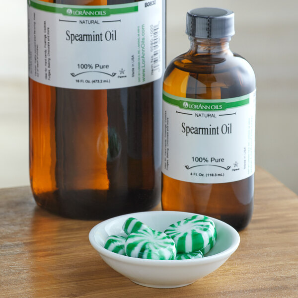 A bottle of spearmint oil next to a bowl of green and white striped candies.