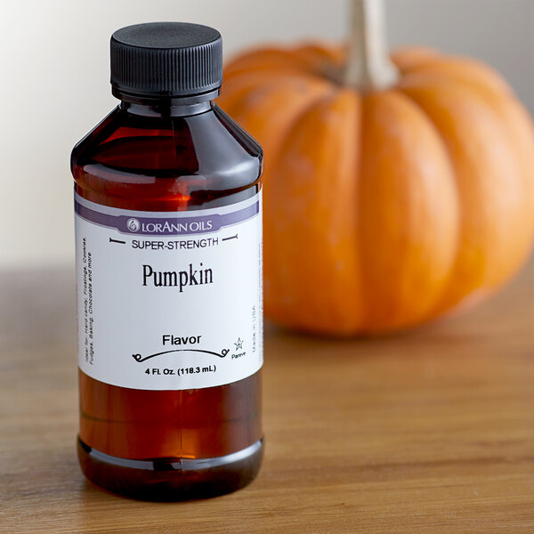 A white labeled bottle of LorAnn Oils Pumpkin Super Strength Flavor liquid next to a pumpkin.