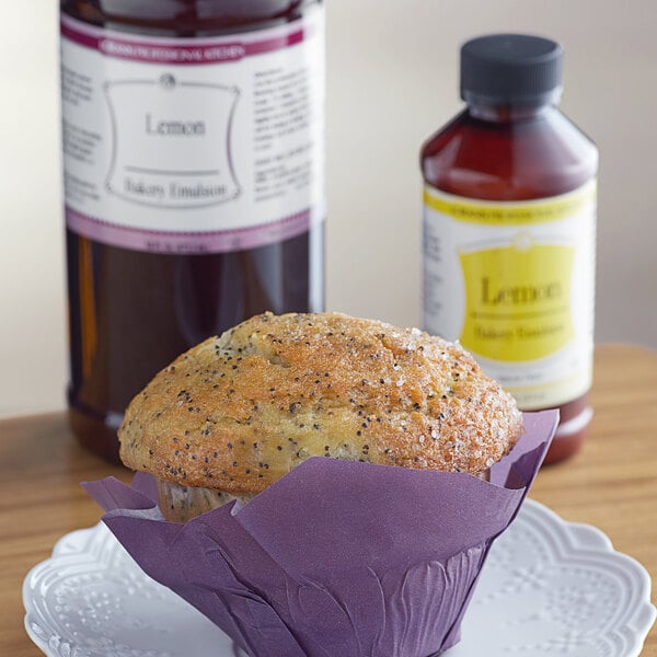A muffin on a plate next to a bottle of lemon emulsion.