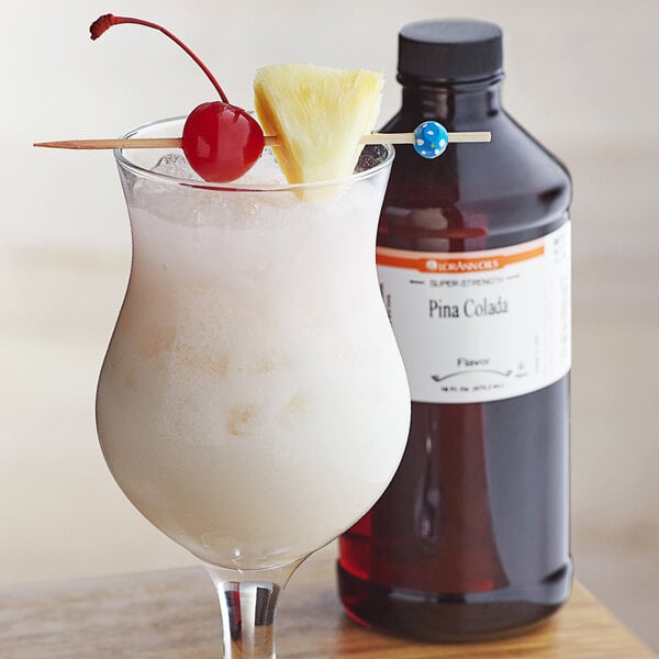 A glass of white liquid with a cherry and pineapple on top next to a bottle of LorAnn Oils Pina Colada flavoring.