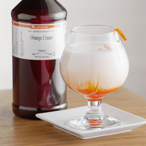 A glass of liquid with orange liquid next to a bottle of LorAnn Oils Orange Cream flavor.