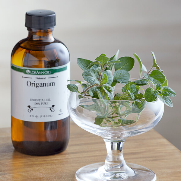 A bottle of LorAnn Oils All-Natural Oregano Super Strength Flavor next to a glass with green leaves in it.