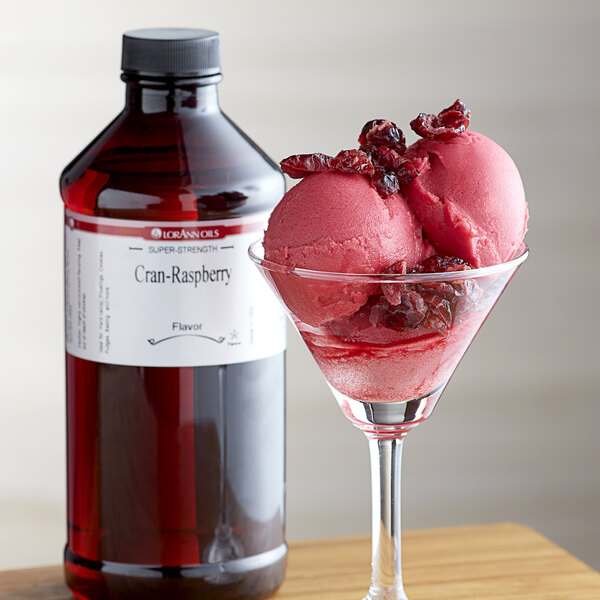 A glass of pink ice cream with cranberries next to a bottle of LorAnn Oils Cran-Raspberry Flavor.