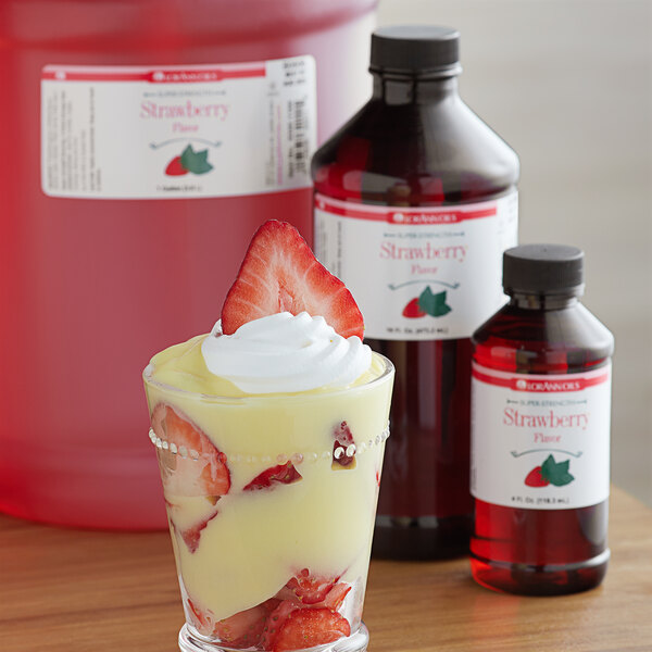 A close-up of a glass of strawberry dessert with strawberries and whipped cream using LorAnn Oils 1 Gallon Strawberry Super Strength Flavor.