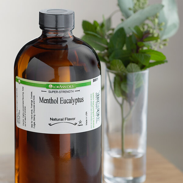 A brown bottle of LorAnn Oils Menthol-Eucalyptus flavor next to a plant in a glass vase.