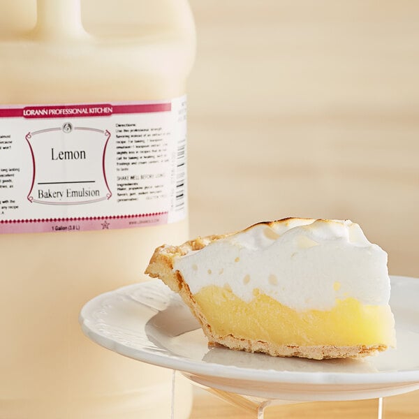 A slice of lemon pie on a plate next to a bottle of LorAnn Oils All-Natural Lemon Bakery Emulsion.