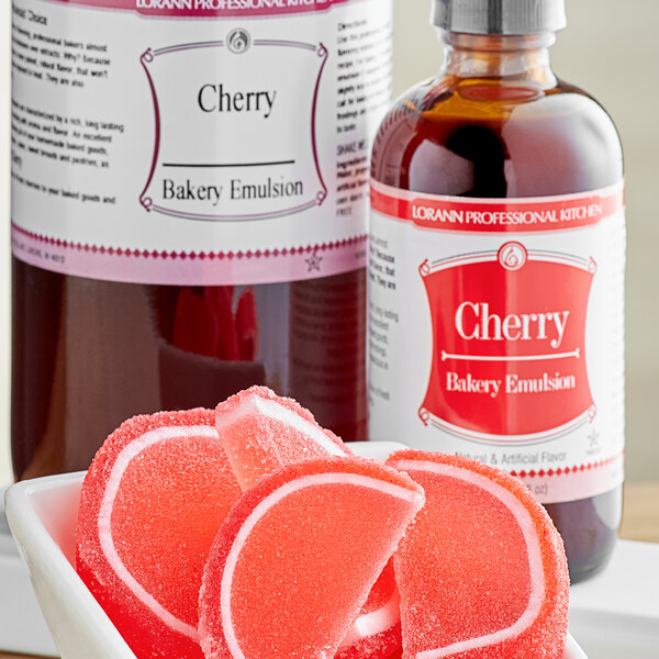 A bottle of LorAnn Oils Cherry Bakery Emulsion on a counter next to a bowl of red candy.