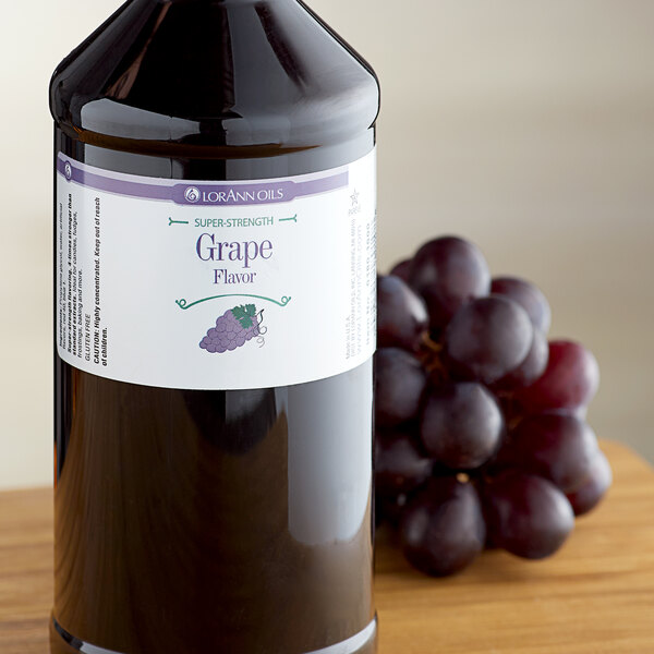 A close-up of a bottle of LorAnn Oils Grape Super Strength Flavor on a table with a bunch of grapes.