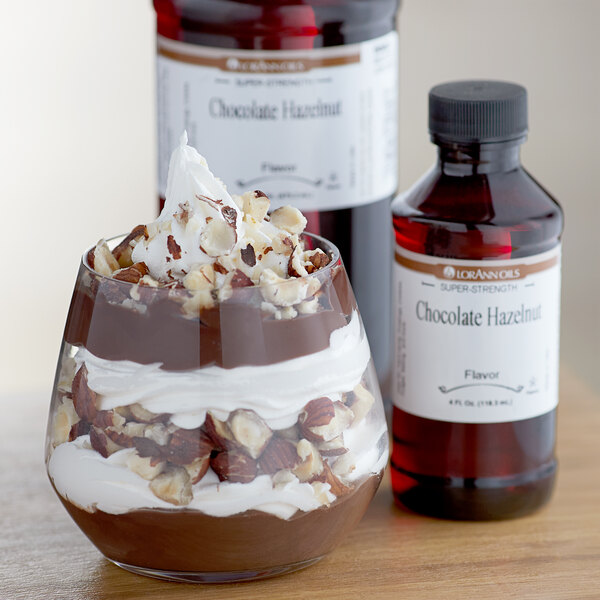 A glass of chocolate dessert with whipped cream and nuts next to a bottle of LorAnn Chocolate Hazelnut flavor.