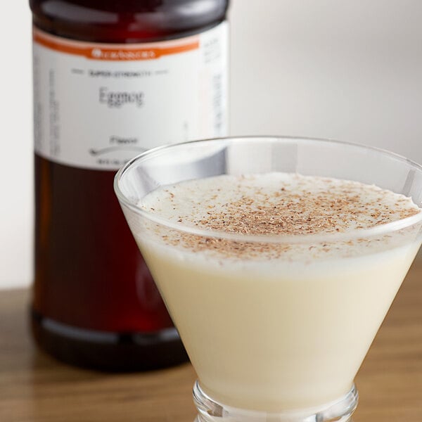 A glass of eggnog with cinnamon on top with a brown bottle of LorAnn Oils Eggnog Super Strength Flavor in the background.