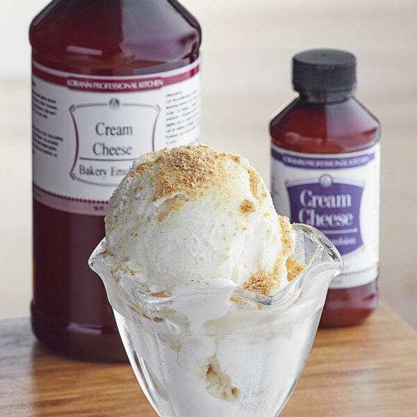 A scoop of ice cream in a glass bowl with a spoon and a jar of LorAnn Cream Cheese Emulsion.