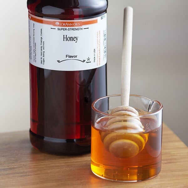A jar of honey next to a glass of liquid with a white label on the bottle.