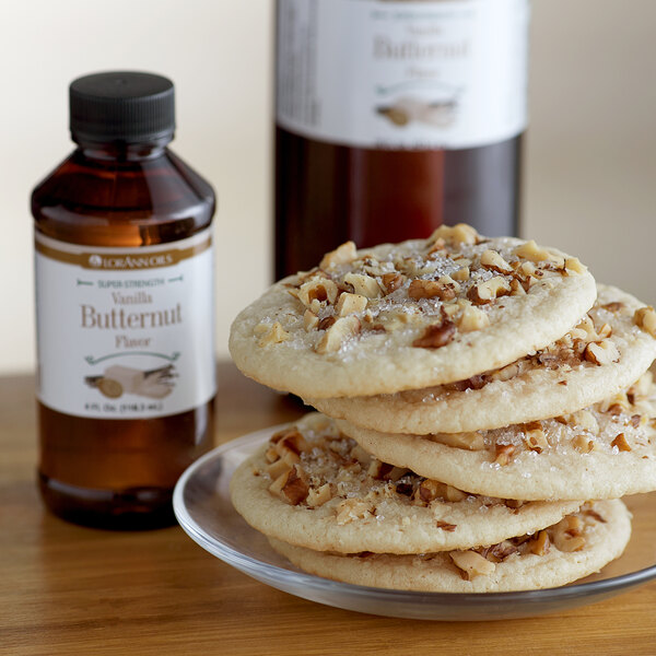 A stack of cookies with nuts on a plate next to a bottle of LorAnn Vanilla Butternut flavor.