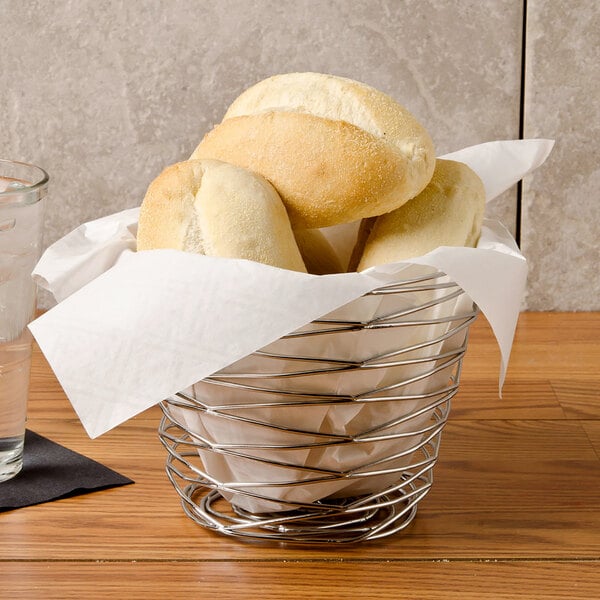 A wire basket with white Bagcraft Packaging sandwich wrap paper holding bread rolls.