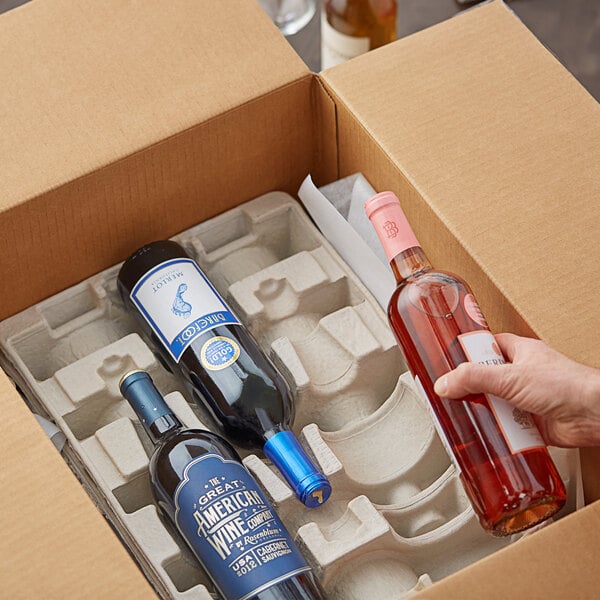 A hand holding a Lavex Molded Fiber 3 bottle wine shipper tray with a bottle of wine inside.