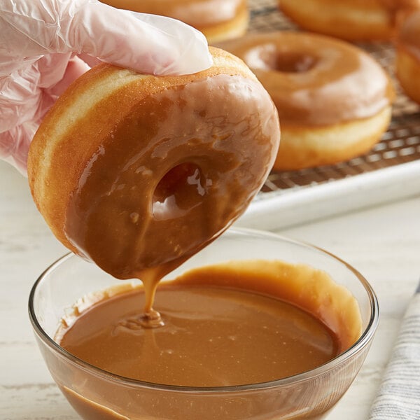 A hand holding a glazed doughnut being dipped into white liquid.