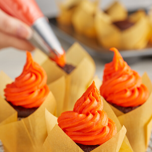 A person using a pastry bag to decorate cupcakes with Rich's Orange Buttrcreme icing.