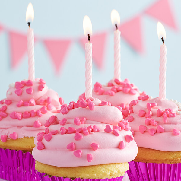 Three cupcakes with Creative Converting iridescent spiral candles on top of pink frosting with sprinkles and small hearts.