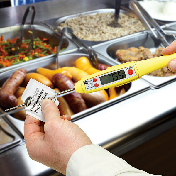 A hand using a yellow Cooper-Atkins thermometer probe wipe on a piece of food.