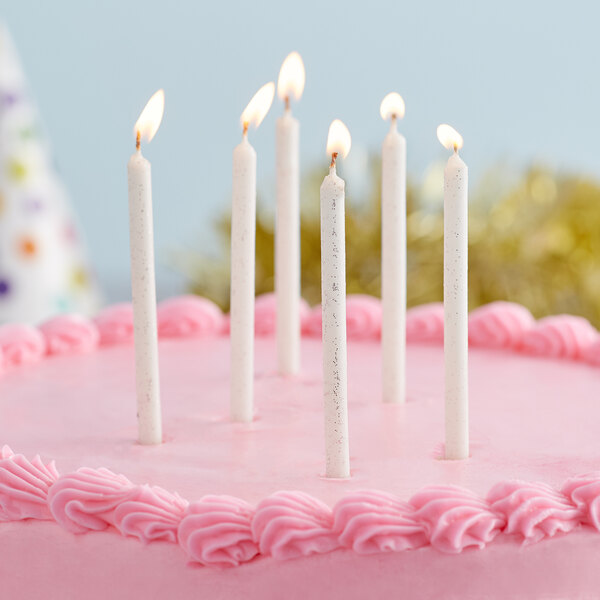 A close up of a pink cake with Creative Converting white tall candles with silver glitter on it.