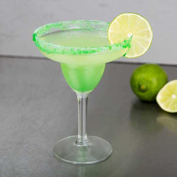 A Libbey margarita glass with a green margarita and a lime wedge on the rim.