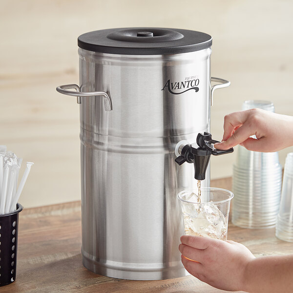 A person using an Avantco stainless steel iced tea dispenser to pour tea into a glass.