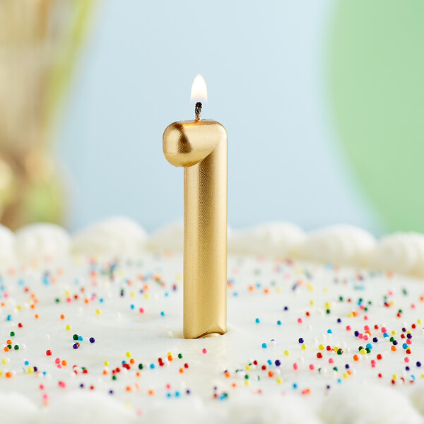 A gold "1" candle on a white cake with colorful sprinkles.