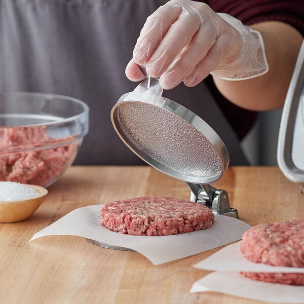 A person using a Choice 4 1/2" Cast Aluminum Hamburger Press to make a raw burger.