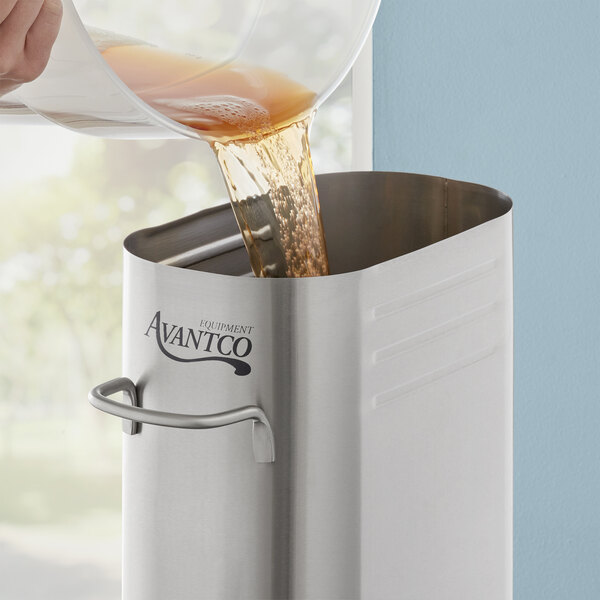 A person pouring brown iced tea into an Avantco stainless steel dispenser.