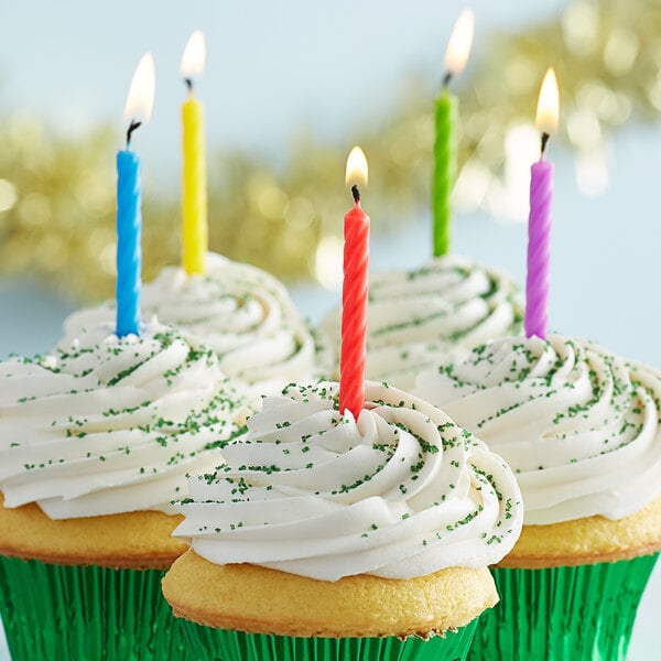 A cupcake with white frosting and rainbow sprinkles with a rainbow spiral candle on top.