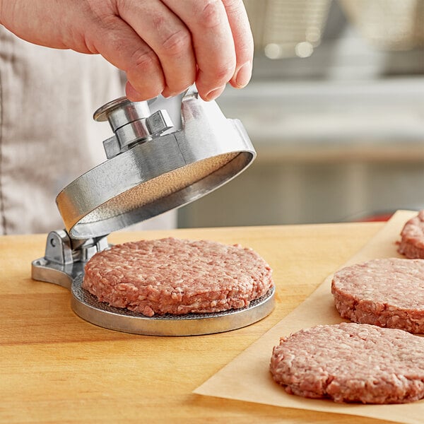 A person using a Choice cast aluminum hamburger press to make a hamburger patty.