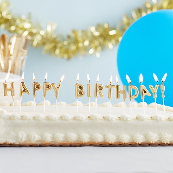A close-up of a birthday cake with gold "Happy Birthday!" candles on top.