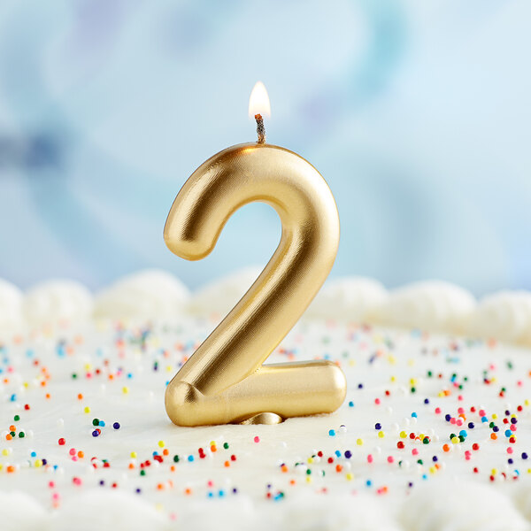 A gold number "2" candle on a cake.