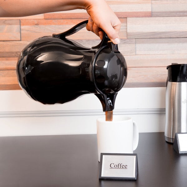 A person pouring coffee from a black Choice Thermal Swirl Coffee Carafe into a mug.