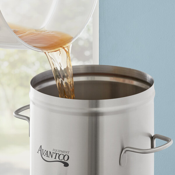 A brown liquid being poured into an Avantco 3 gallon iced tea dispenser.